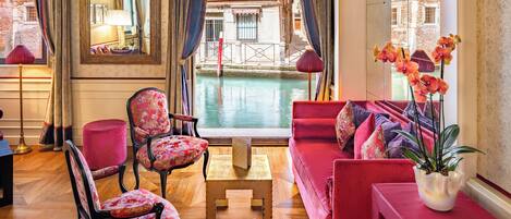 Habitación con sofá rojo, sillas con estampado floral, una pequeña mesa de madera y vista a un canal.