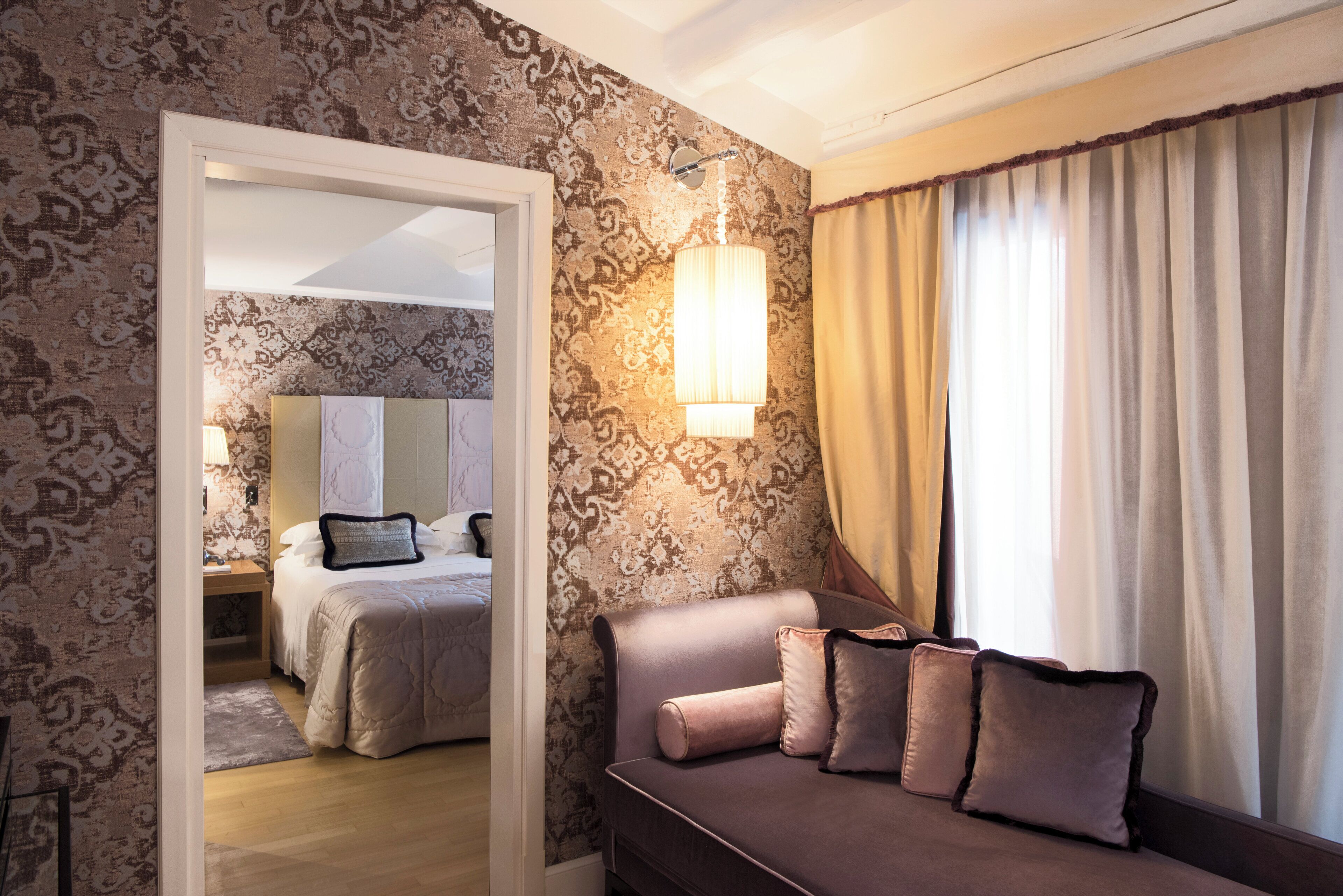 A hotel room with a bed, a sofa, a lamp, and a view of another room through a doorway.