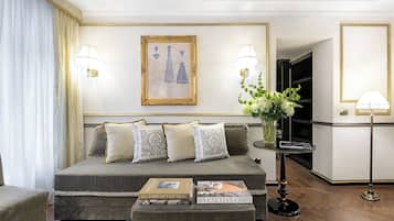 Habitación de hotel elegante con una cama grande, una mesita de noche con libros, un florero con flores y dos lámparas de pared.