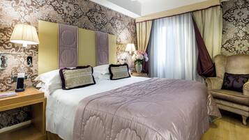 A hotel room with a large bed, a nightstand with a lamp, a chair, and a wall with patterned wallpaper.