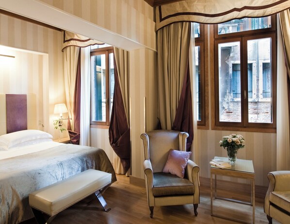 A hotel room with a bed, a chair, a small table with a vase of flowers, and curtains over the windows. - Splendid Venice – Starhotels Collezione (Venice)