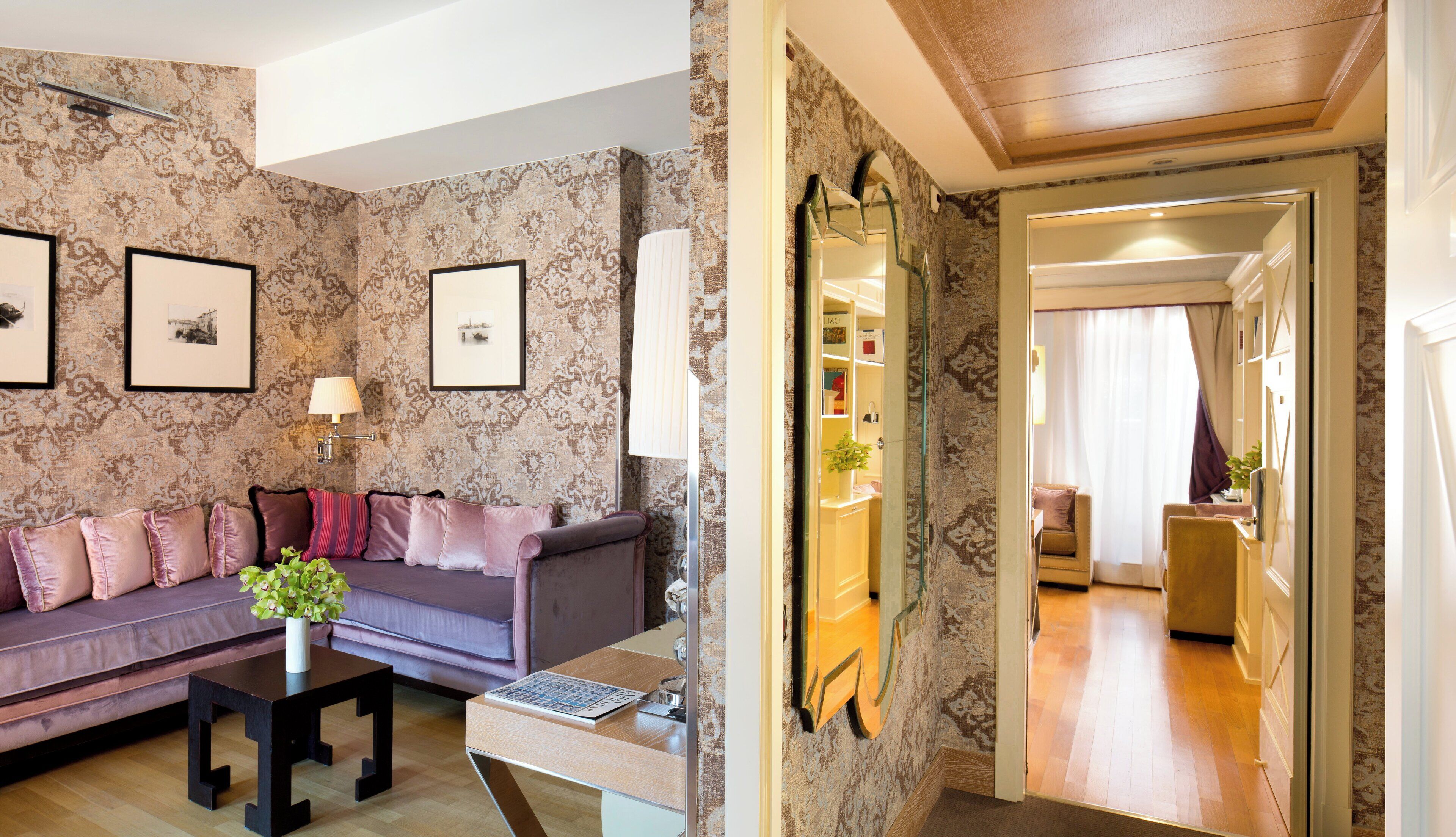 A living room with a sofa, a table, and a lamp. There is a mirror on the wall and a door leading to another room.