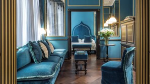 Una habitación con un sofá azul, un reposapiés a juego, una cama con cabecera azul y un espejo.