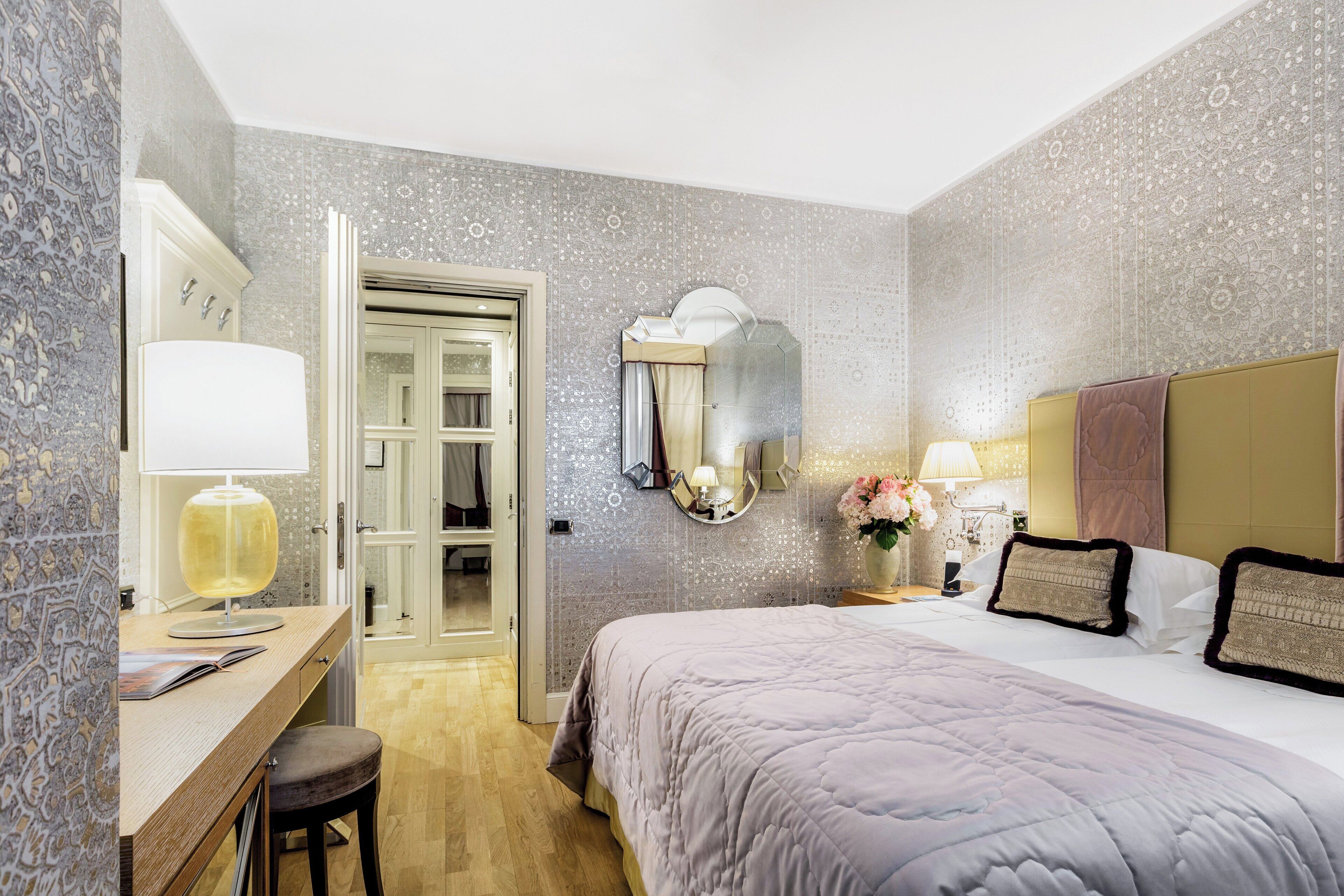 Una habitación de hotel con una cama, mesita de noche, lámpara y espejo.