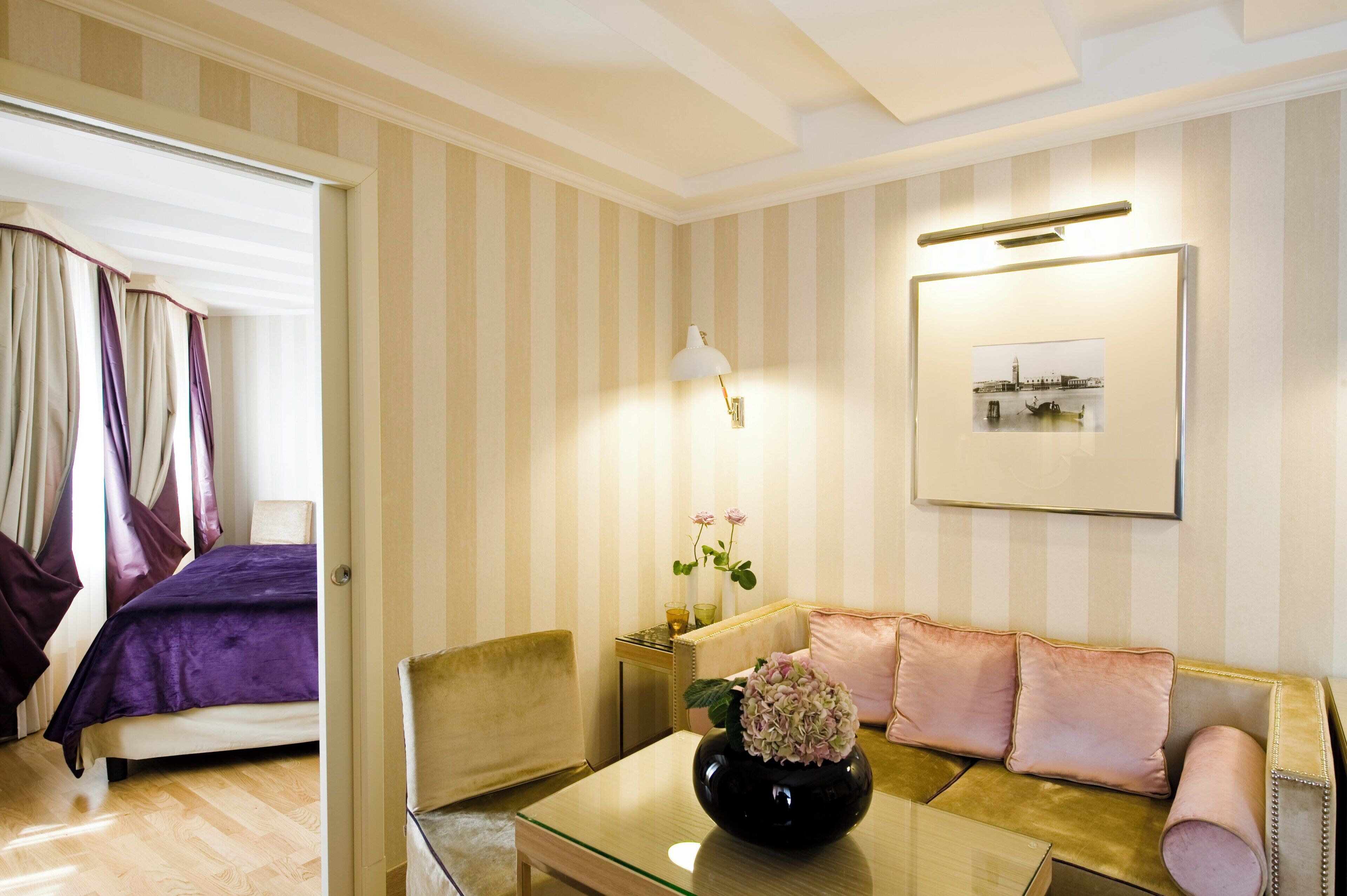 A hotel room with a bed, a sofa, a coffee table with a vase, and a wall-mounted lamp.