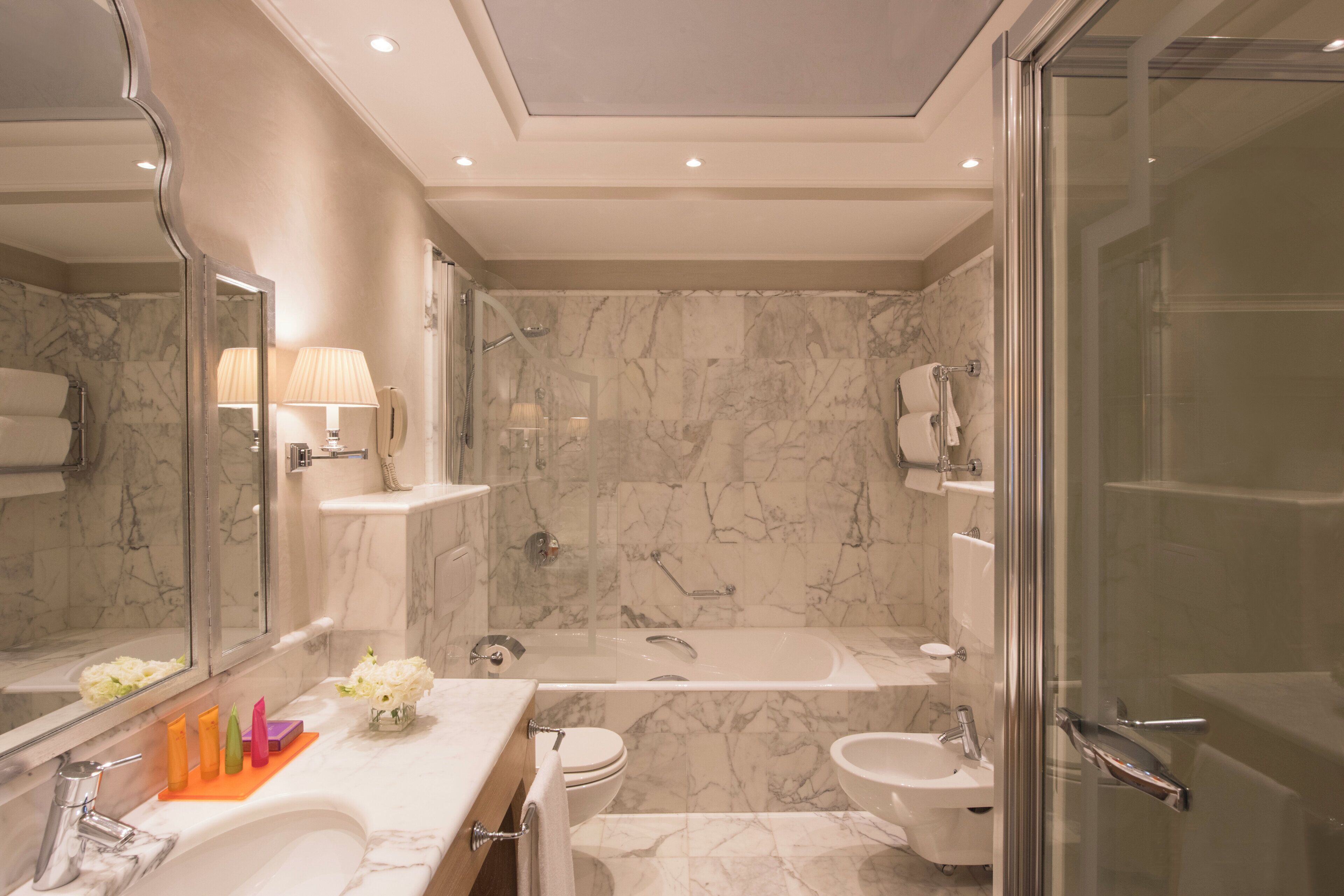 A modern bathroom with a marble shower, a bathtub, a toilet, and a bidet.