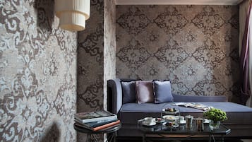 Un moderno salón con papel tapiz estampado, un sofá con cojines, una mesa de centro con libros y un jarrón, y una lámpara.