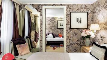 Une chambre d’hôtel avec un lit, une chaise, une valise, un miroir, une lampe et un vase de fleurs.