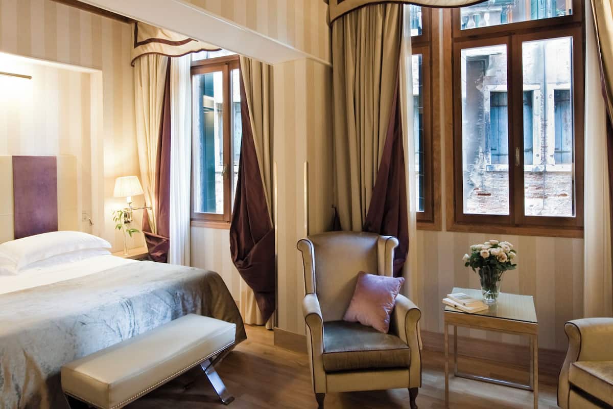 A hotel room with a bed, a chair, a small table, and curtains.