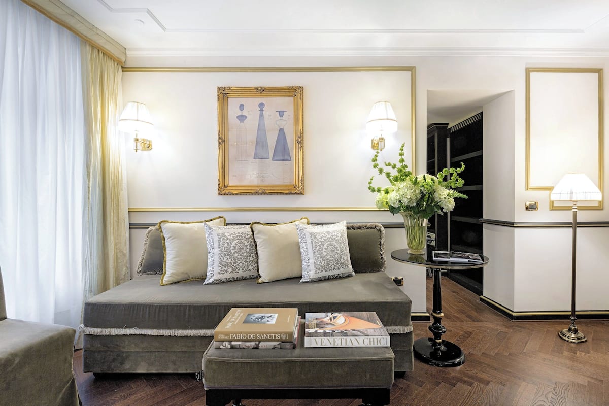 A well-appointed hotel room with a large bed, a side table with books, a vase with flowers, and two wall-mounted lamps.