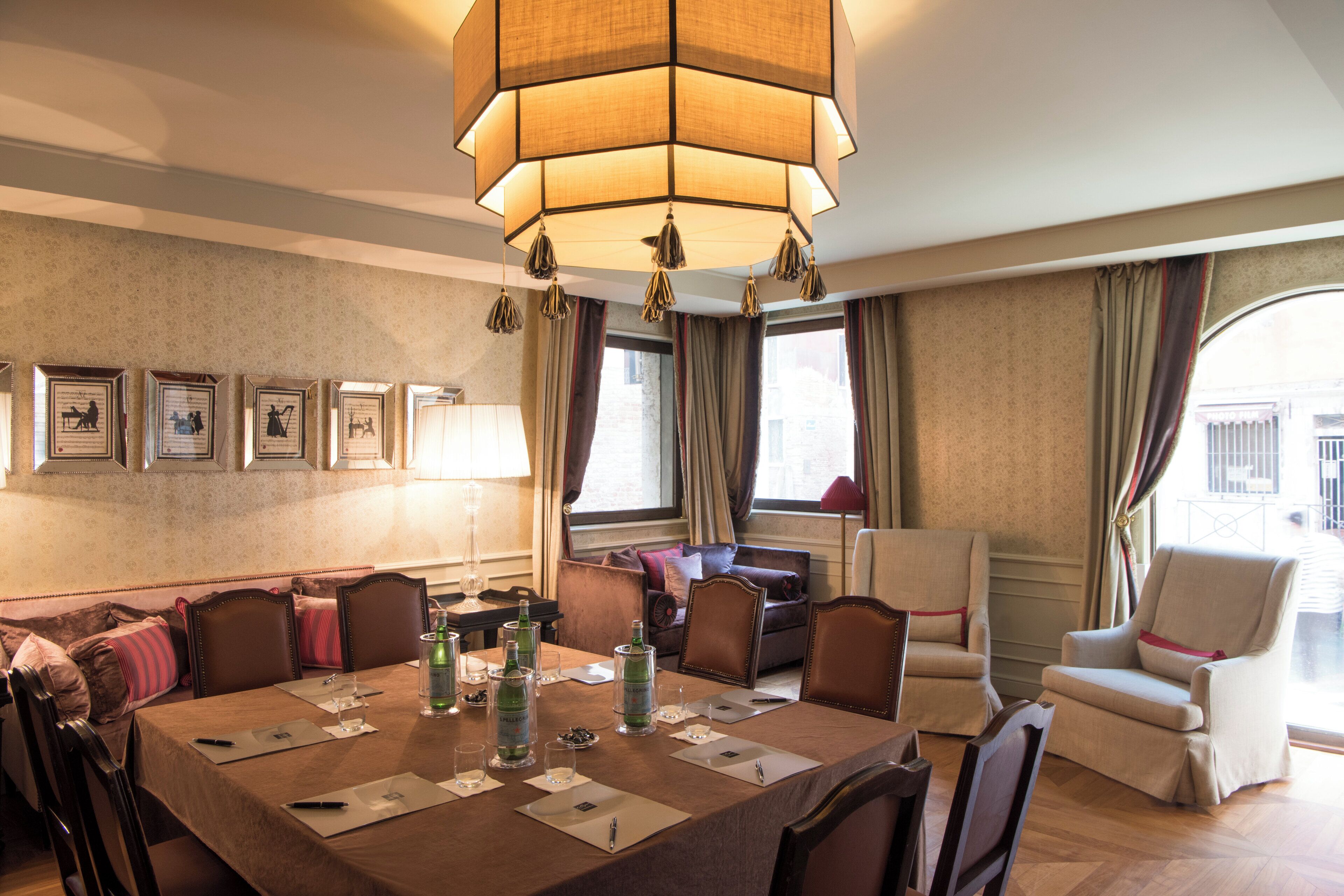 A hotel dining area with a large table set for a meeting, surrounded by comfortable seating and a large hanging light fixture.