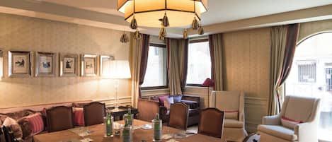 A hotel dining area with a large table set for a meeting, surrounded by comfortable seating and a large hanging light fixture.