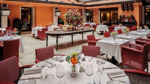Un restaurante con mesas redondas, sillas de mimbre rojas y un arreglo floral central.