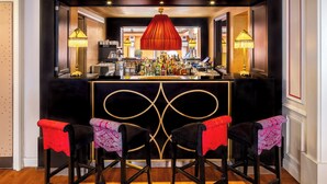 Zona de bar con mostrador negro, dos taburetes con fundas estampadas en rojo y rosa, y una lámpara colgante roja.