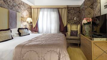 A hotel room with a large bed, a chair, a dresser, a TV, and a window with curtains.