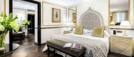 Un dormitorio de hotel con una cama grande, mesitas de noche, un banco y un espejo.