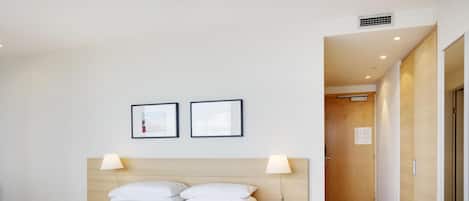 A hotel room with a bed, two bedside lamps, a nightstand, and a wooden headboard.