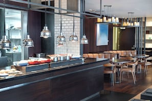 A modern kitchen with stainless steel appliances, a bar area with stools, and pendant lighting. - Hilton Reykjavik (Reykjavik)