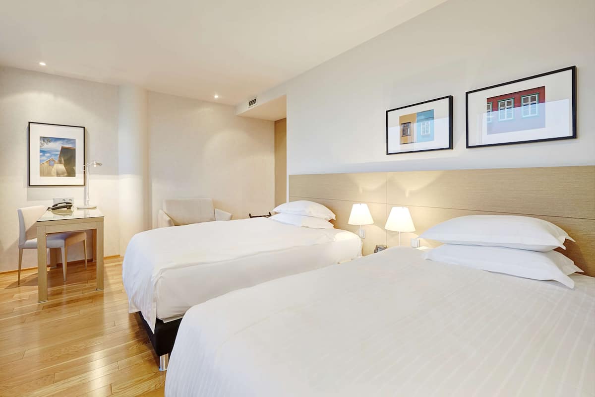 A hotel room with two beds, a desk, and a chair. There are framed pictures on the wall.