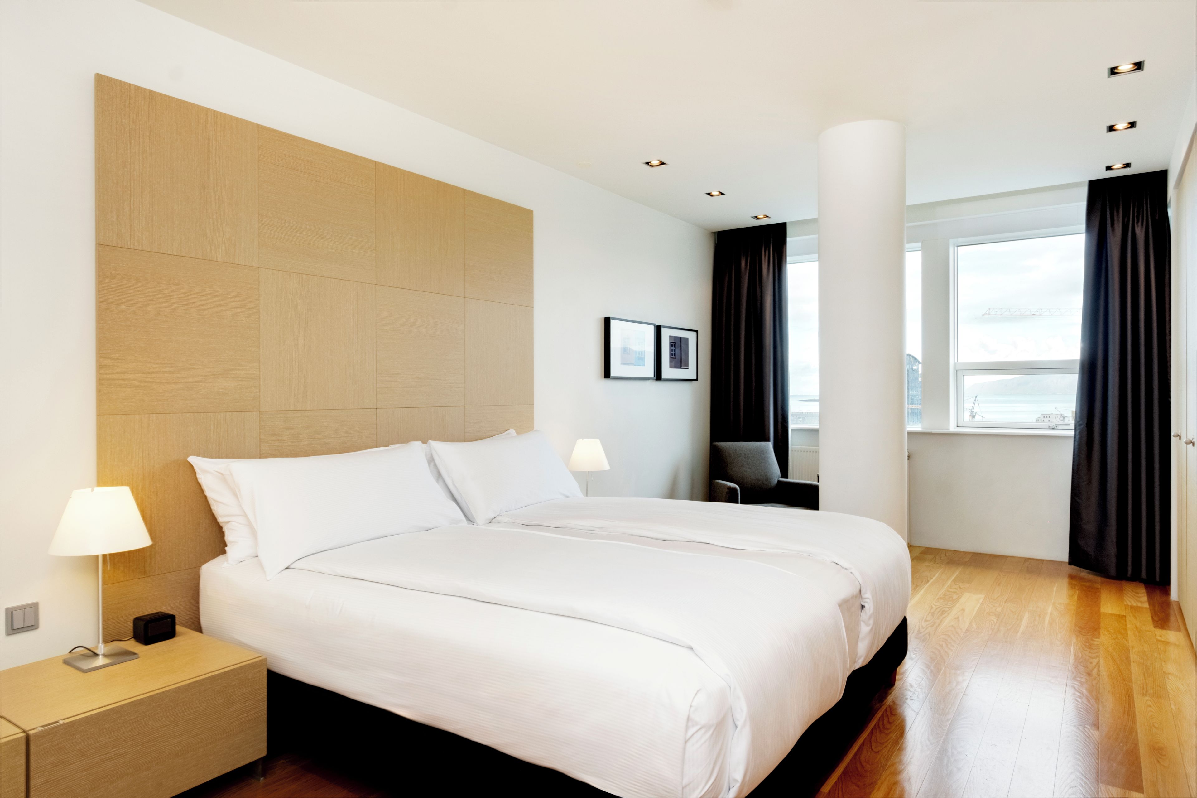 Ett modernt hotellrum med en stor säng, sängbord, ett skrivbord och ett fönster med gardiner.