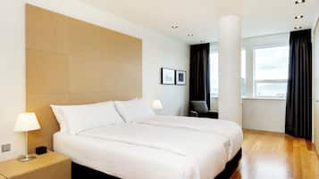 Quarto de hotel moderno com uma cama grande, mesas de cabeceira, escrivaninha e uma janela com cortinas.