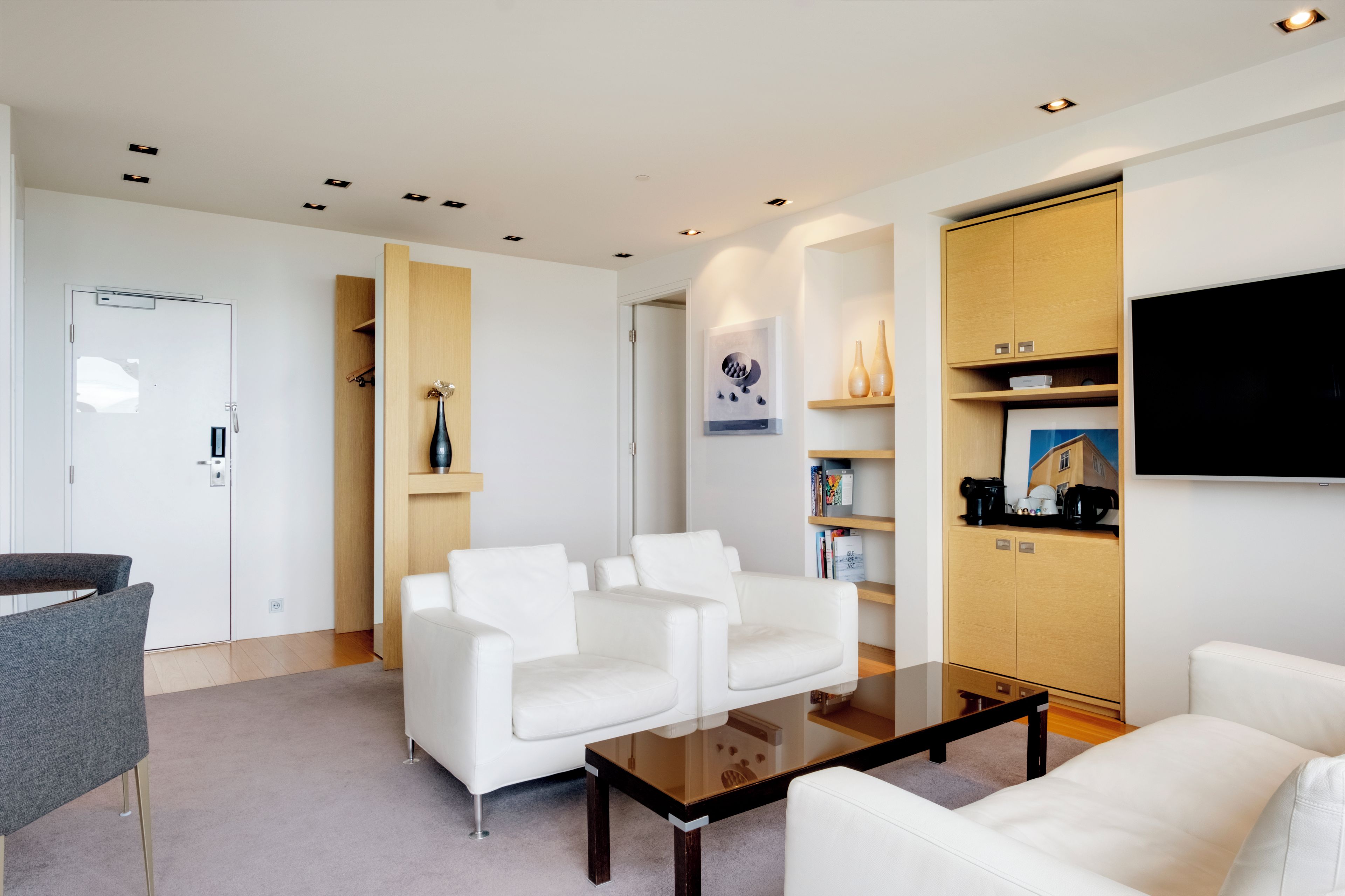 A modern living room with white sofas, a glass coffee table, and built-in wooden shelving with books and decorative items.