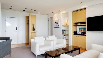 A modern living room with white sofas, a glass coffee table, and built-in wooden shelving with books and decorative items.