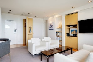A modern living room with white sofas, a glass coffee table, and built-in wooden shelving with books and decorative items. - Hilton Reykjavik (Reykjavik)
