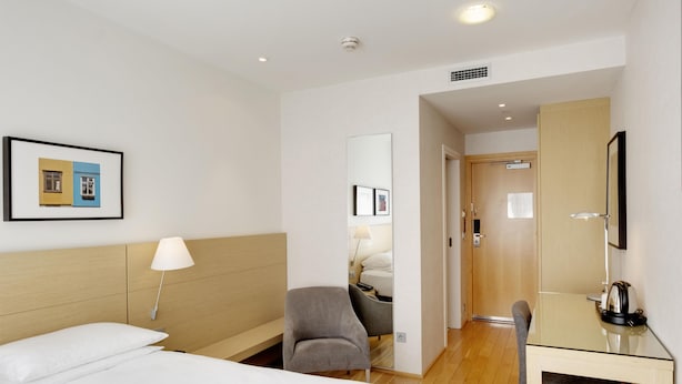 A hotel room with a bed, a desk, a chair, a lamp, a mirror, and a picture on the wall. - Hilton Reykjavik (Reykjavik)