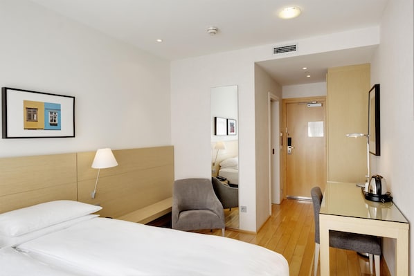 A hotel room with a bed, a desk, a chair, a lamp, and a mirror. - Hilton Reykjavik (Reykjavik)