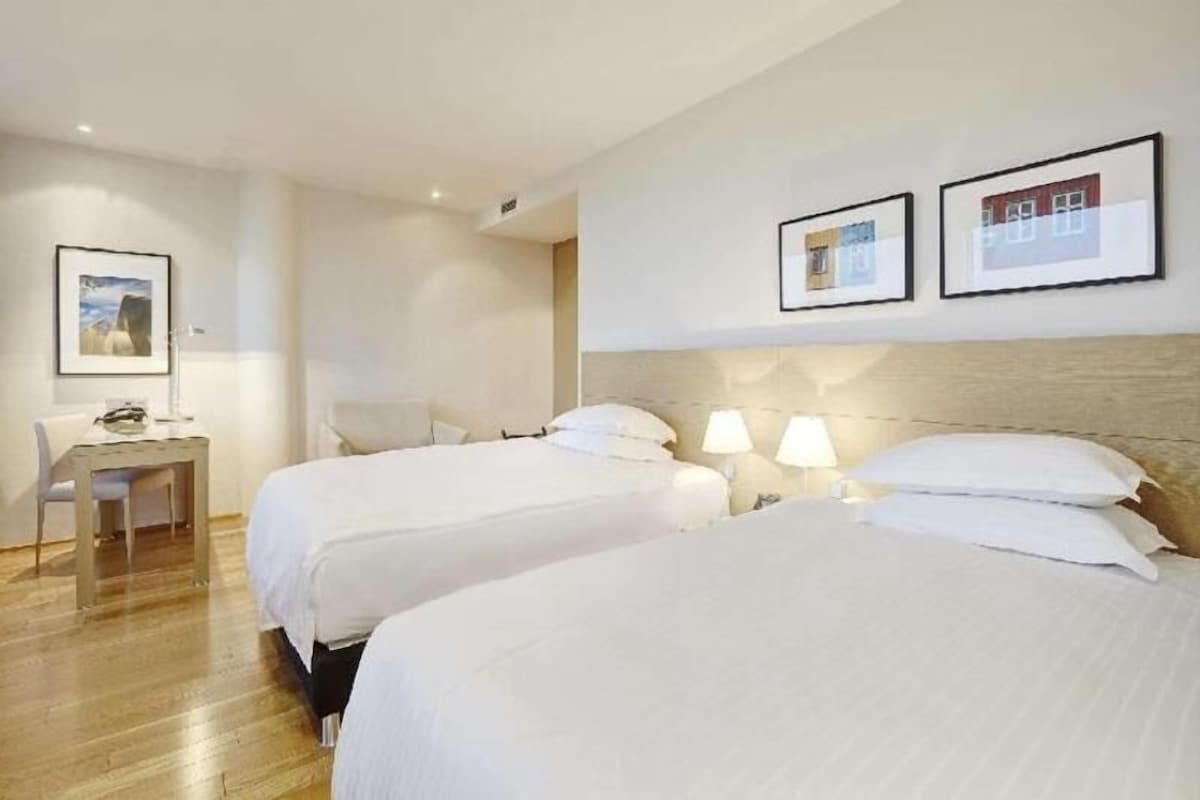 A hotel room with two beds, a desk, and a chair. There are framed pictures on the wall.