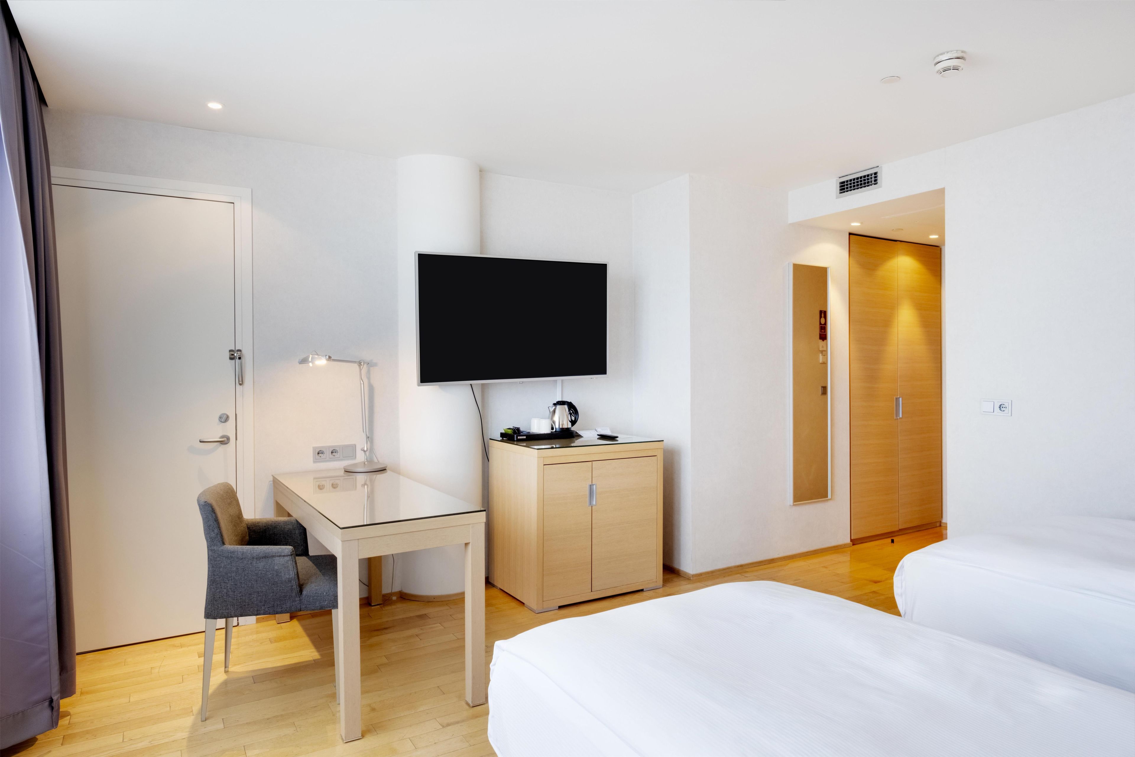 Una habitación de hotel con una cama, un escritorio, una silla, un televisor y un armario.
