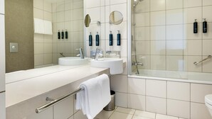 A modern bathroom with a bathtub, two sinks, a mirror, and a shower. - Hilton Reykjavik (Reykjavik)