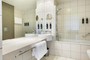A modern bathroom with a bathtub, two sinks, a mirror, and a shower. - Hilton Reykjavik (Reykjavik)