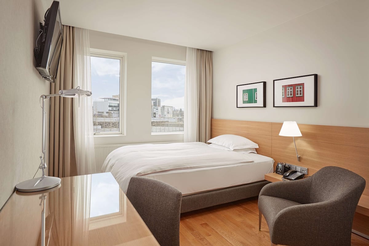 A hotel room with a bed, bedside table, lamp, chair, TV, and two framed pictures on the wall.