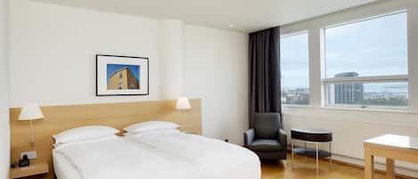 A hotel room with a large bed, a chair, a small table, a picture on the wall, and a window with a view.