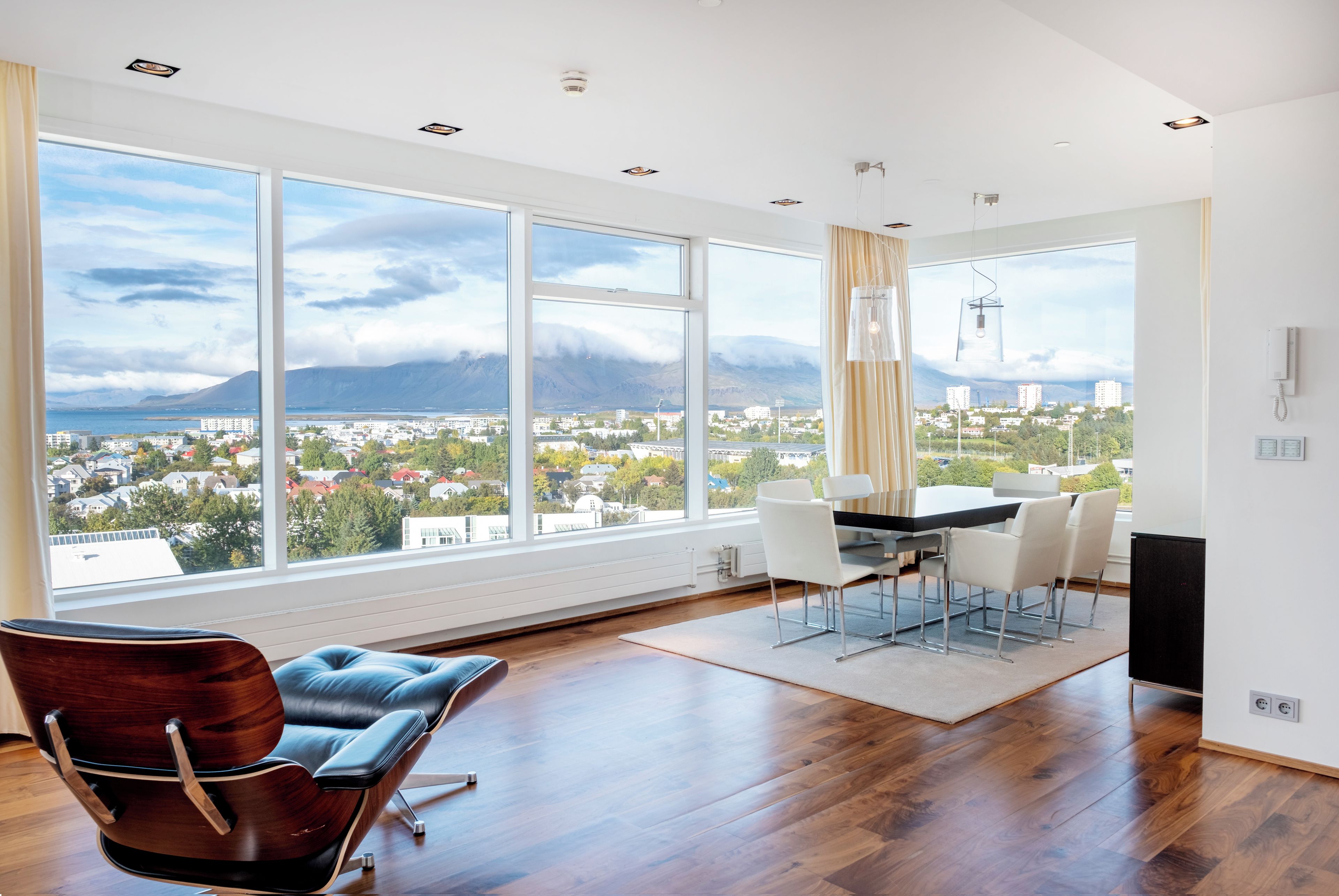 A spacious room with a large window offering a city view, a dining area with a table and chairs, and a modern chair.