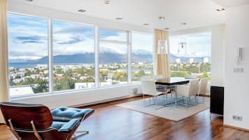 A spacious room with a large window offering a city view, a dining area with a table and chairs, and a modern chair.