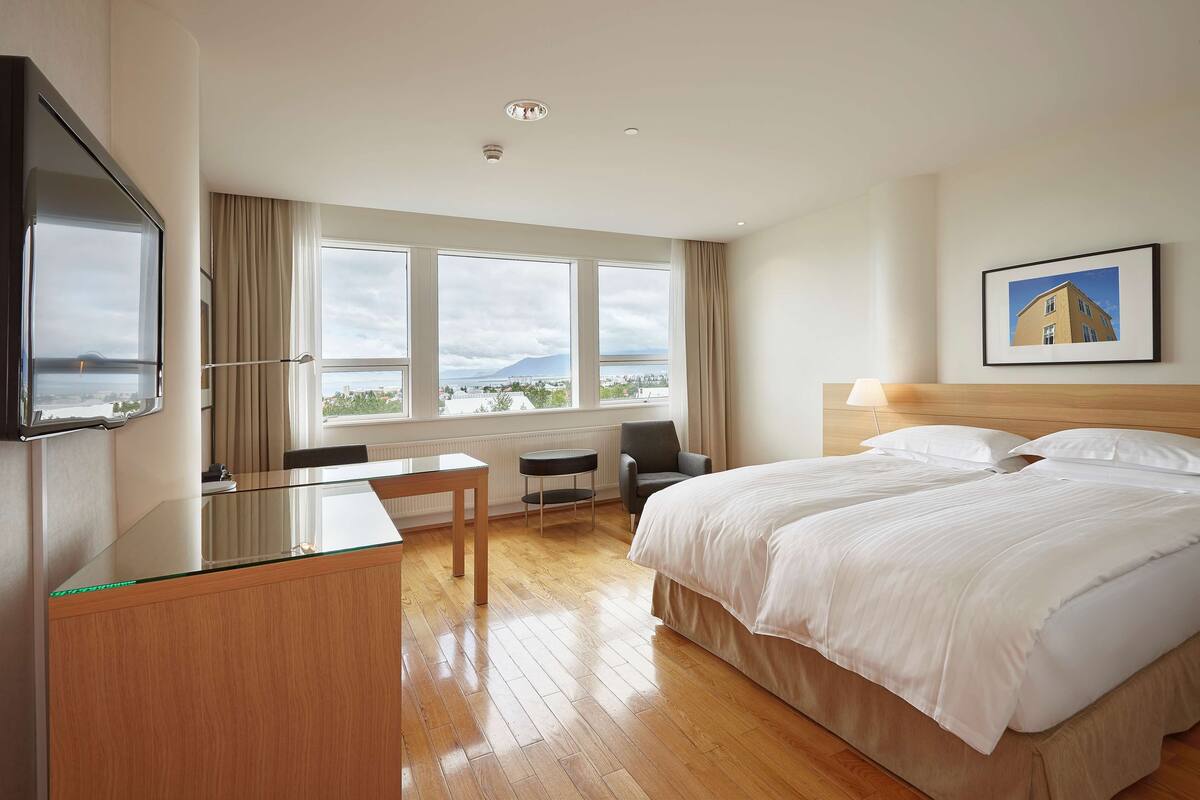A hotel room with a large bed, a desk, a chair, and a TV.