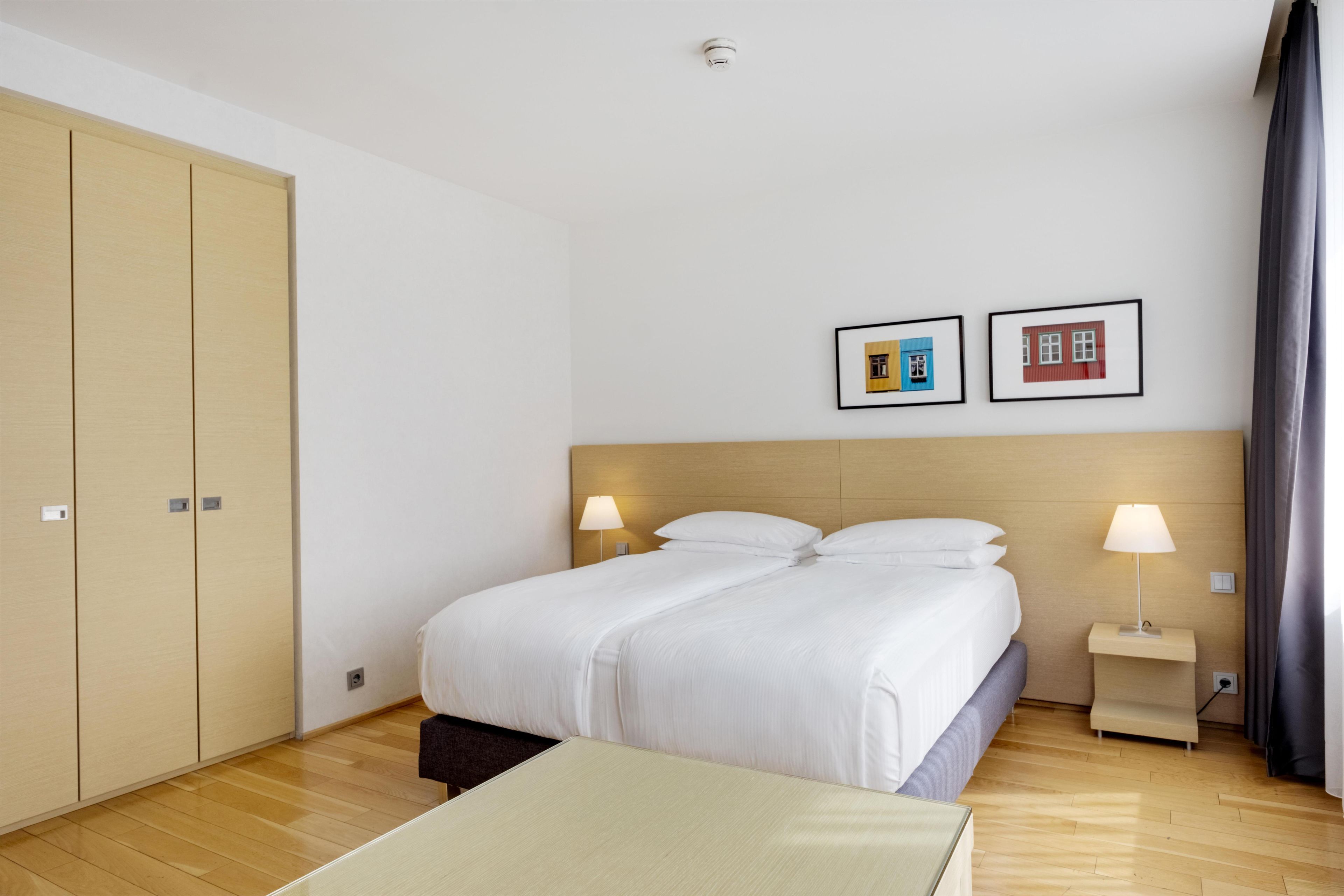 Ett hotellrum med en stor säng, sänglampor, en garderob och två inramade tavlor på väggen.