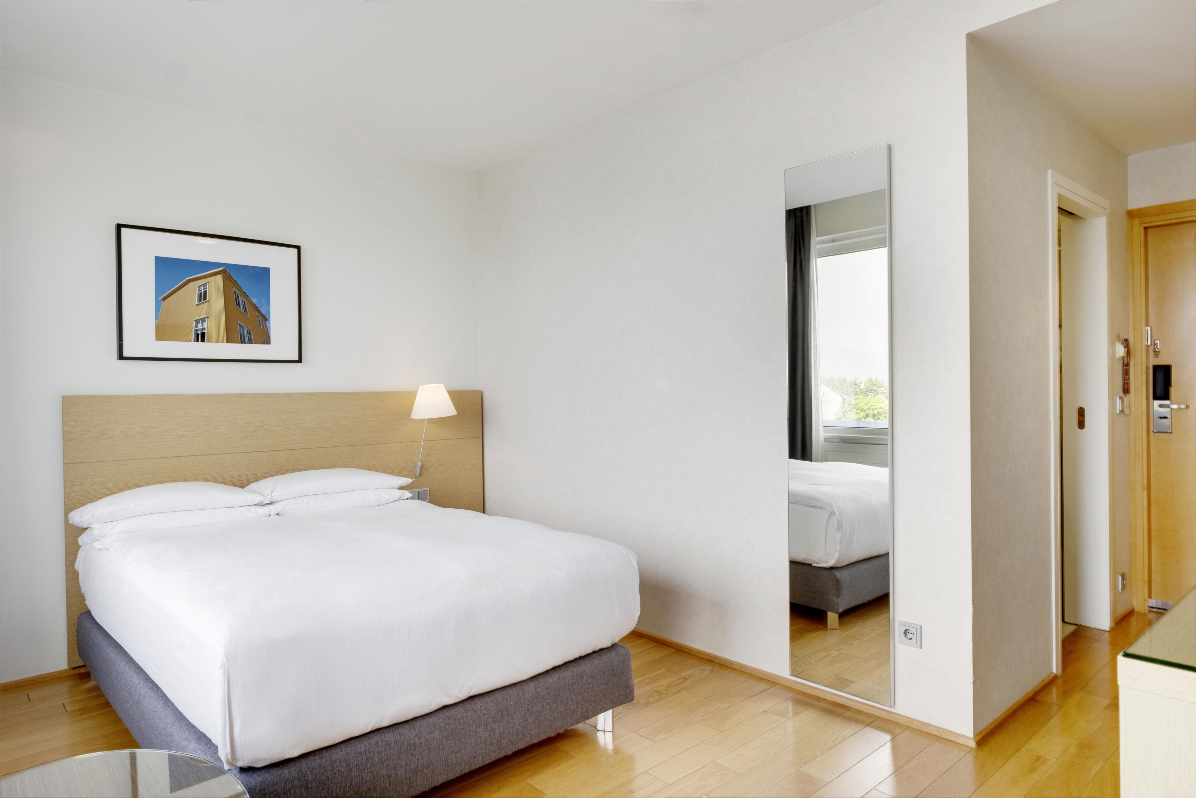 Quarto de hotel com cama, luminária de cabeceira, quadro na parede e espelho refletindo o ambiente.