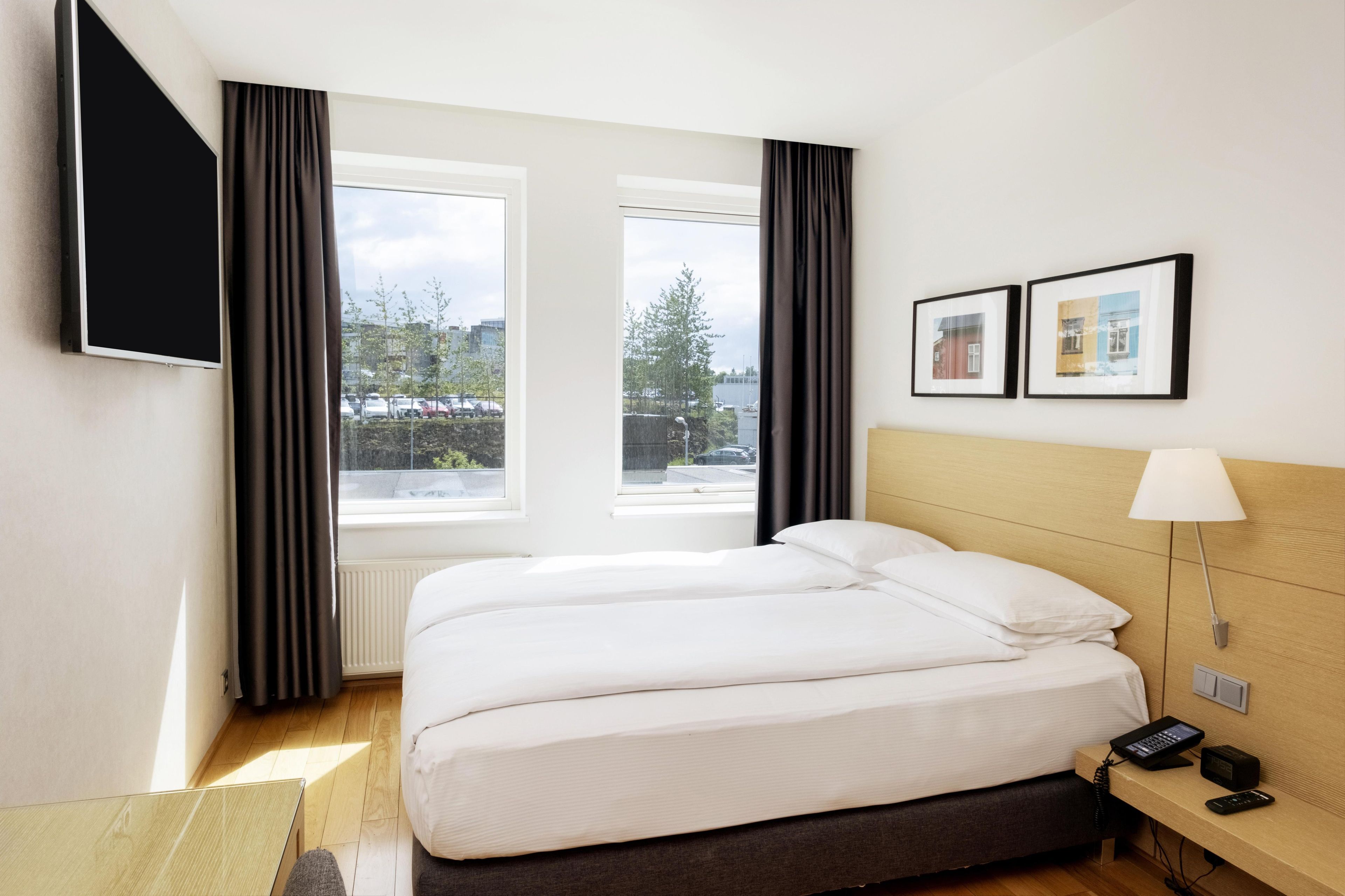 Habitación de hotel con cama, escritorio con lámpara, teléfono y televisor en la pared.
