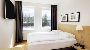 Habitación de hotel con cama, escritorio con lámpara, teléfono y televisor en la pared.