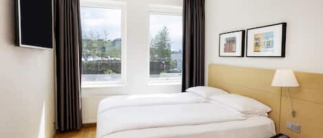 Habitación de hotel con cama, escritorio con lámpara, teléfono y televisor en la pared.