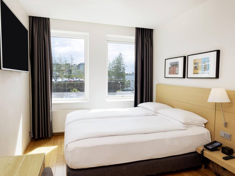A hotel room with a bed, a desk with a lamp, a phone, and a TV on the wall.