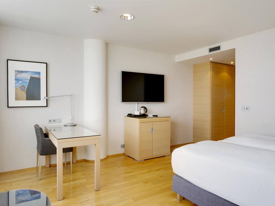 Habitación de hotel con cama, escritorio con silla, televisor, armario y un cuadro en la pared.