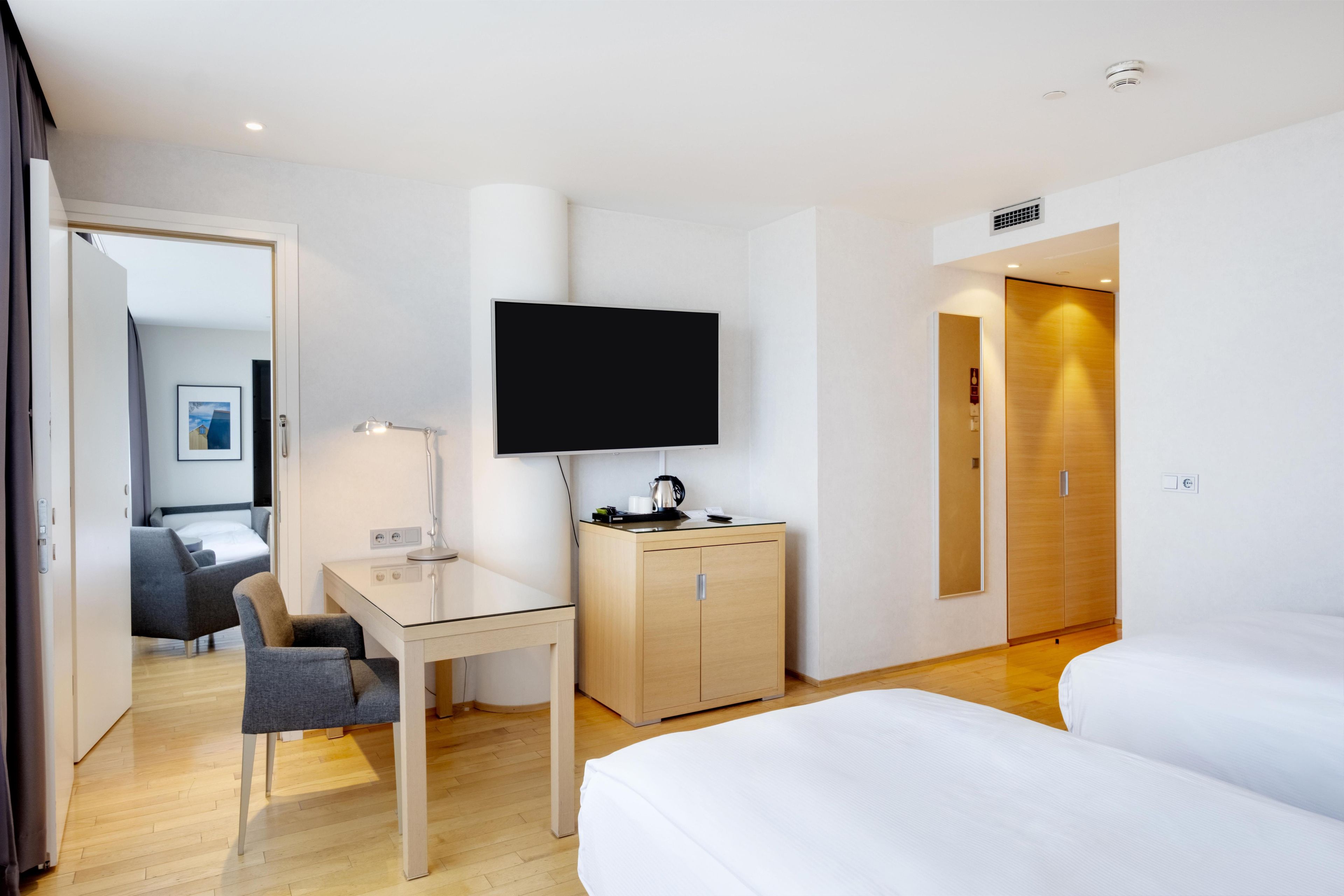 A hotel room with a bed, a desk with a chair, a television, a wardrobe, and a door leading to another room.