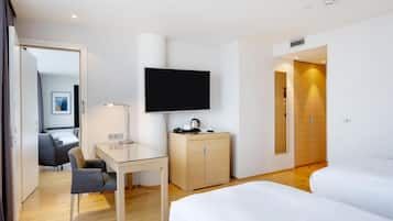 A hotel room with a bed, a desk with a chair, a television, a wardrobe, and a door leading to another room.