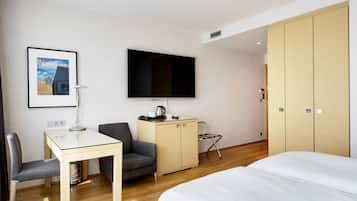A hotel room with a bed, a desk with a chair, a television, a wardrobe, and a framed picture on the wall.
