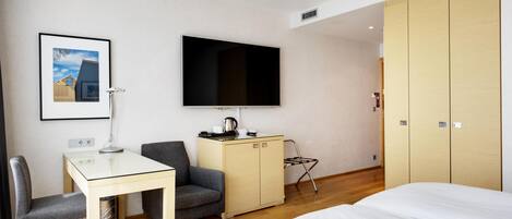 Habitación de hotel con cama, escritorio con silla, televisión, armario y un cuadro en la pared.